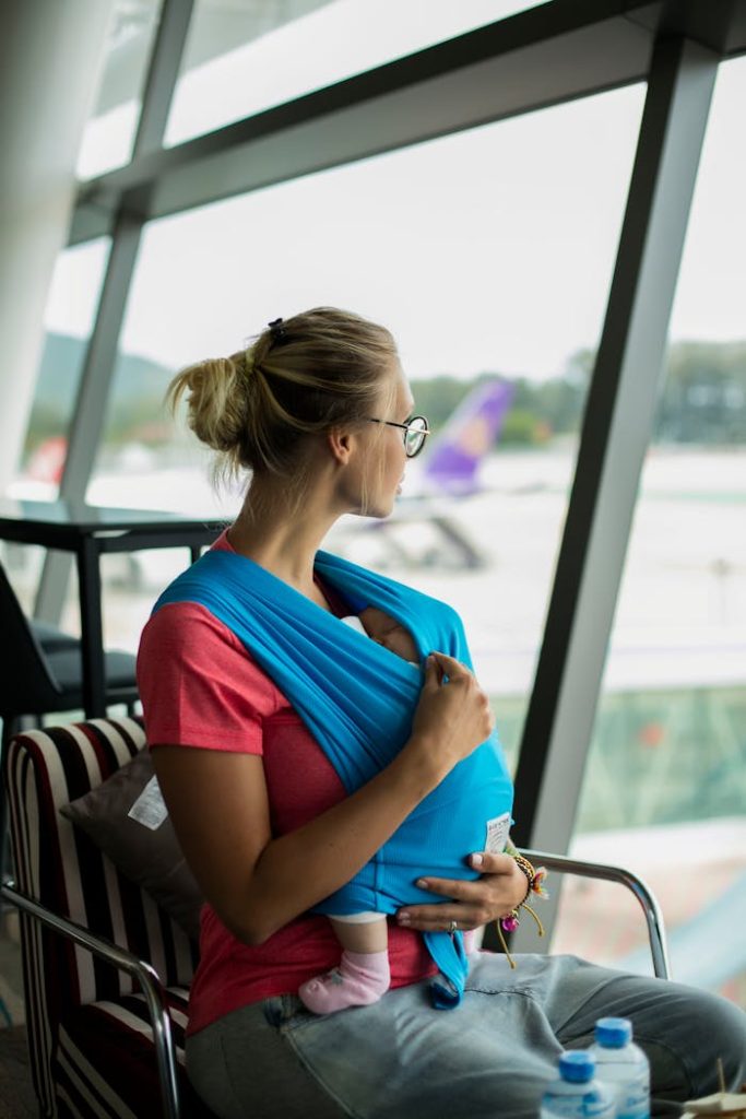 A mother with her baby in a sling looks out the window at Phuket airport.