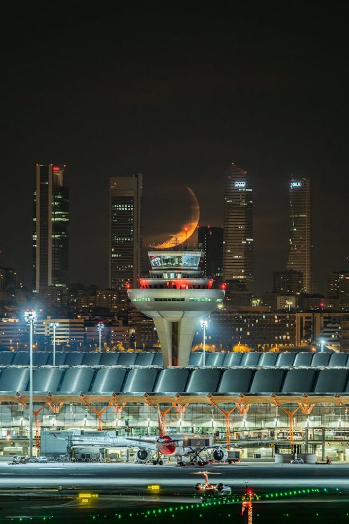 Stunning nighttime view of Madrid airport with illuminated skyline and crescent moon.