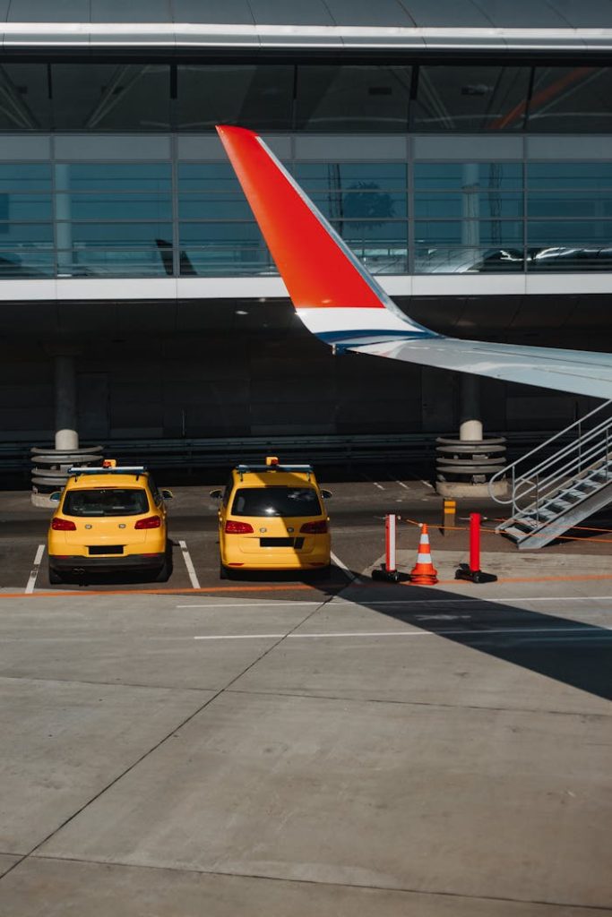 Two yellow taxis parked under an airplane wing at an urban airport.